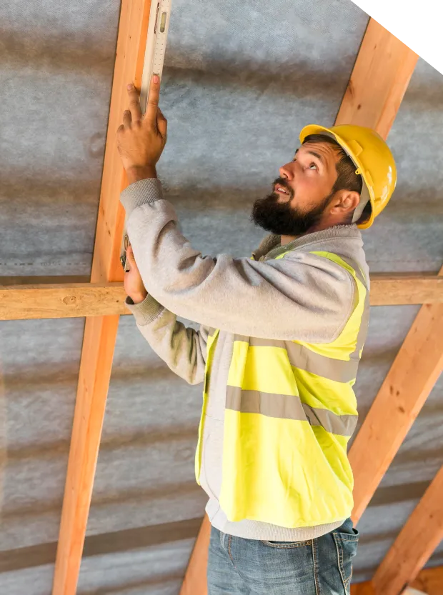 Construction worker measuring wooden beams in attic