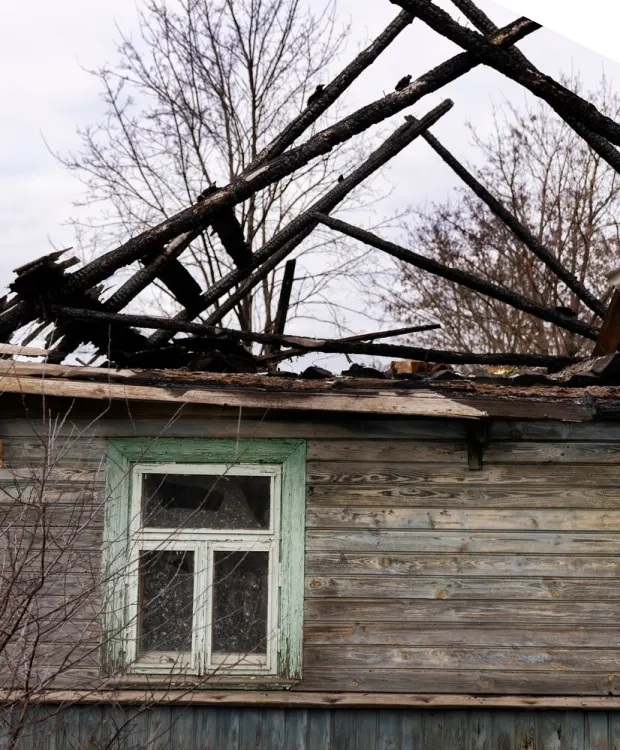 Burned wooden house with damaged roof structure.