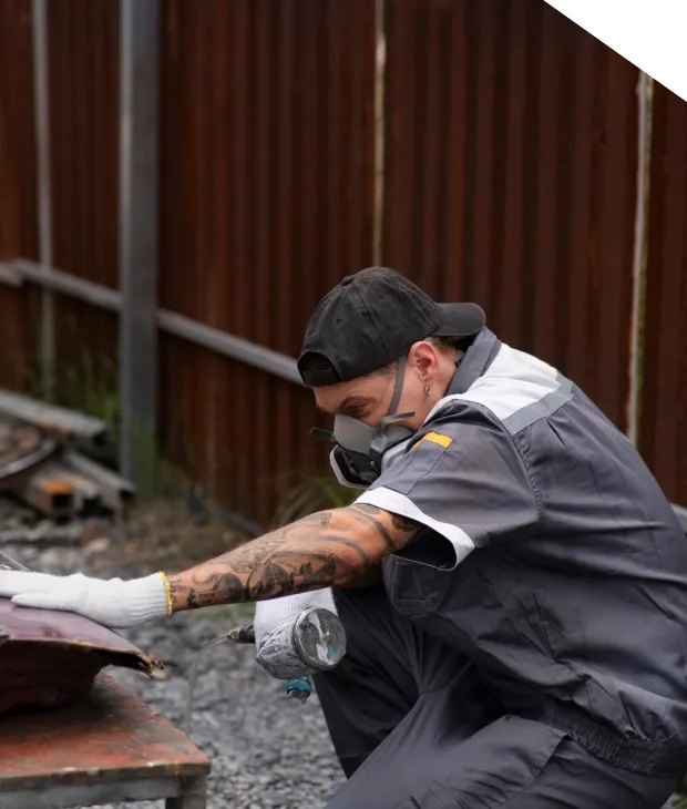 Person sanding wooden surface outdoors with mask