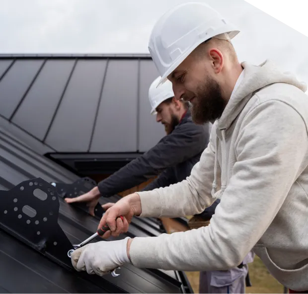 Roofers installing metal roof panels with tools.